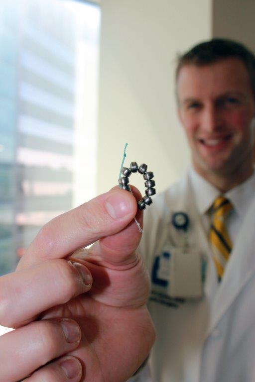 Dr. Shawn Groth stands in the background holding the LINX® System device, a small, flexible band of magnets enclosed in titanium beads implanted in to treat GERD.