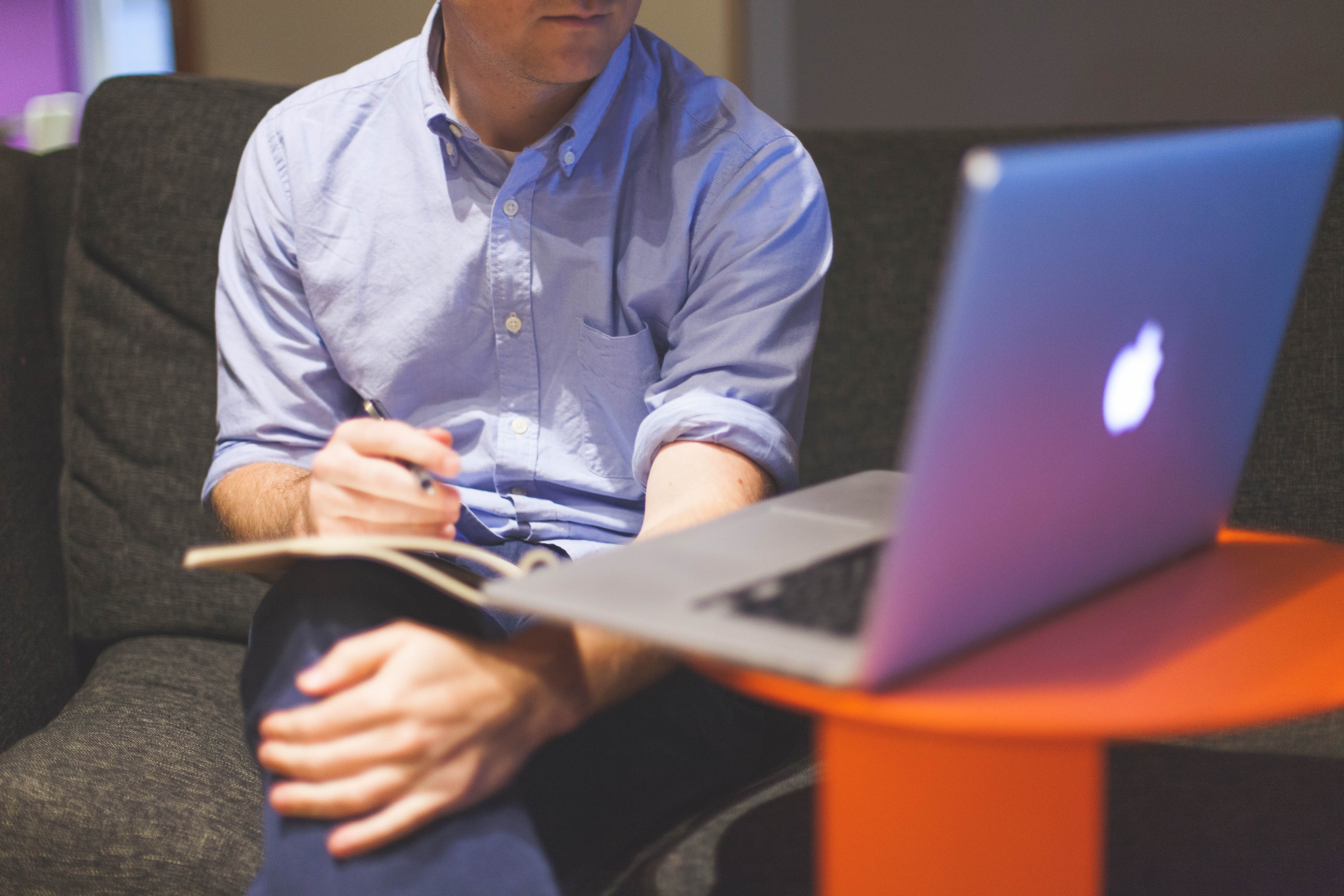 A man sits in front of a computer writing in a notebook