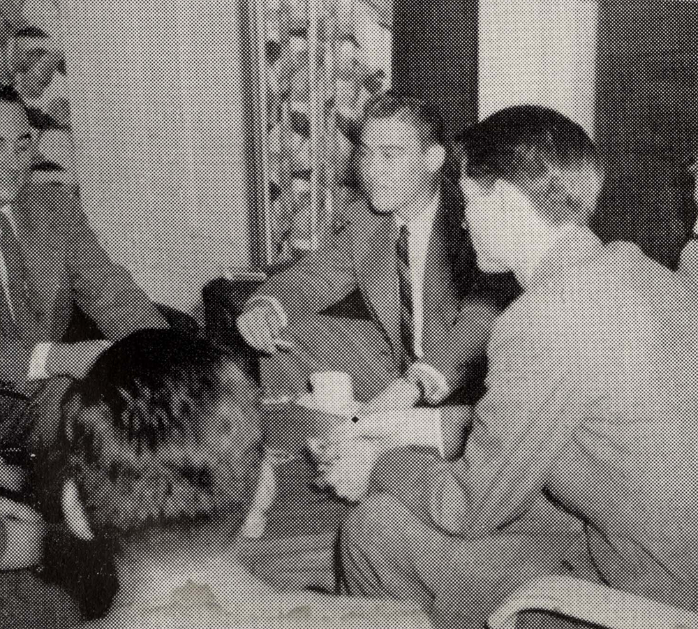 A group of well-dressed men sitting around a table, talking and laughing.