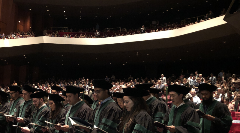 A crowd of graduating medical schools taking an oath in front of an audience.