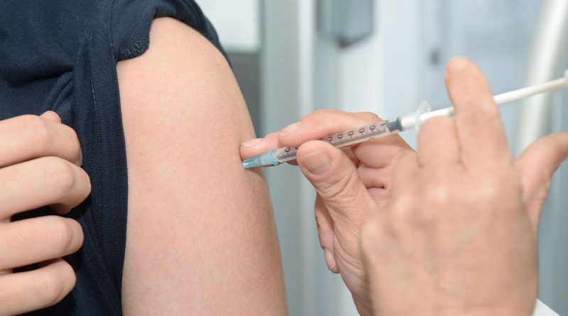 A flu vaccine needle being put into an arm.