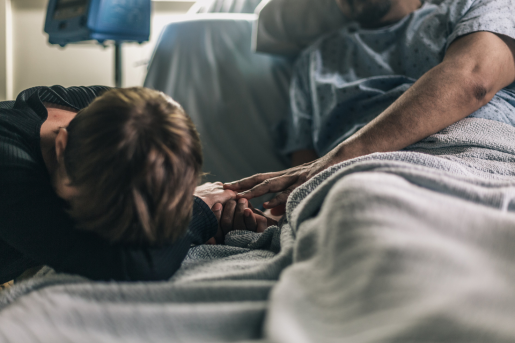 woman-lays-head-on-hospital-bed-while-patient-comforts-her-final