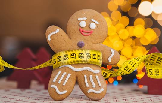A gingerbread person cookie wearing measuring tape around their stomach.
