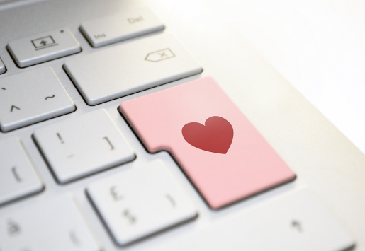 A computer keyboard with a pink key that has a red heart instead of a character..