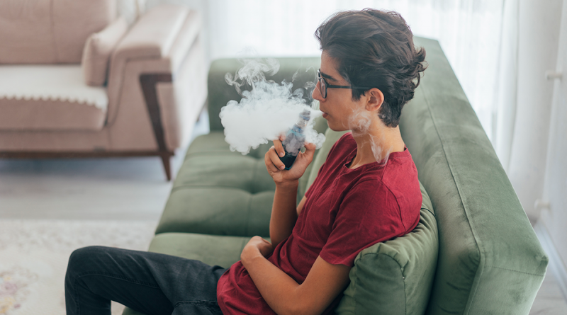 A young person sitting on a couch while vaping.