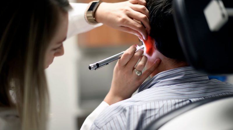 An audiologist looks into a patients ears with an otoscope.