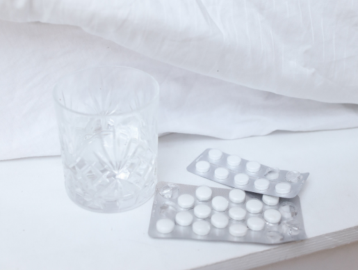 Some pills and a glass of water sitting next to a bed.