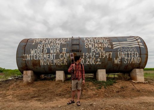 Musician Julian Saporiti stands in front of a large metal tank with the words "Justice for All" and various examples of unjust actions the American government has taken painted on it.