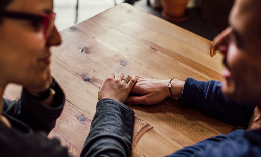 Two people, sitting at a table, holding hands and talking