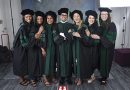 Graduates from the class of 2022 stand together while wearing their green and black graduation robes. The group is posing inside a photo studio.