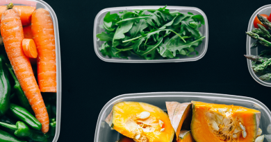 A selection of cut fruits and veggies, including leafy greens, carrots and a melon, sitting in small plastic containers on a black surface.