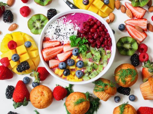 A colorful collection of fruits, vegetables, nuts and muffins laid out on a table and inside a bowl.