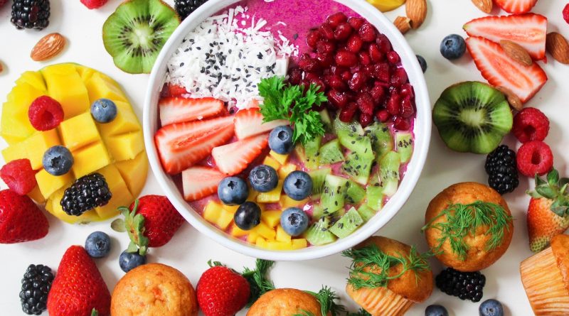 A colorful collection of fruits, vegetables, nuts and muffins laid out on a table and inside a bowl.