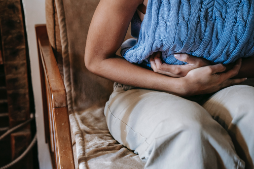 A person sitting on a chair while doubled over in pain and clutching their abdomen.