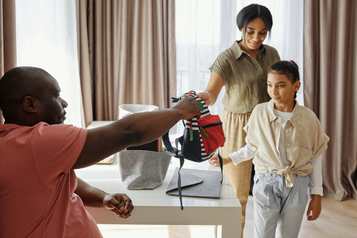 Two parents handing a backpack to their child as they prepare for the first day of school.