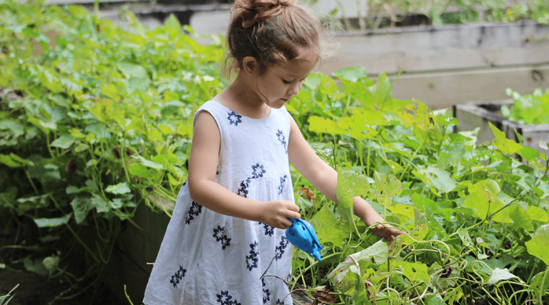 A child in a white dress holds a tool in a large garden.