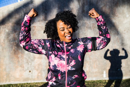 A woman in purple and pink workout gear celebrating with arms up in a flex pose.