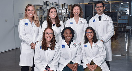 Seven members of the pediatrics critical care fellowship pose in their white coats