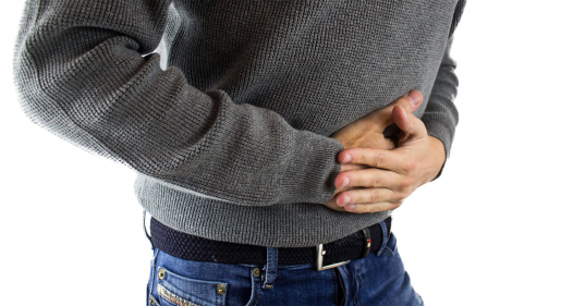 A person wearing jeans and a sweater is doubled over in pain, clutching their stomach.