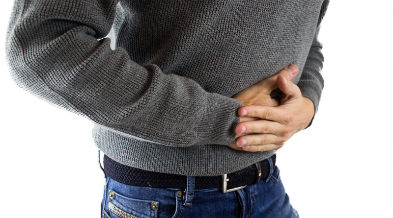 A person wearing jeans and a sweater is doubled over in pain, clutching their stomach.