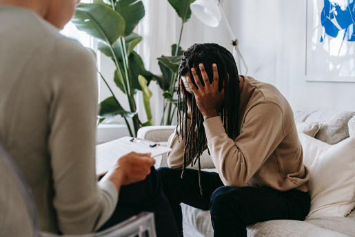 A patient with long dreadlocks holds their head in their hands while sitting in front of a therapist.