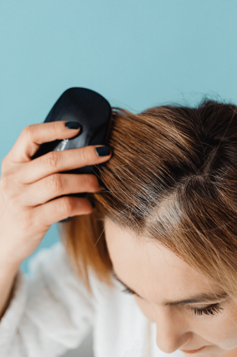 A woman with black-painted nails moves a comb through her hair.