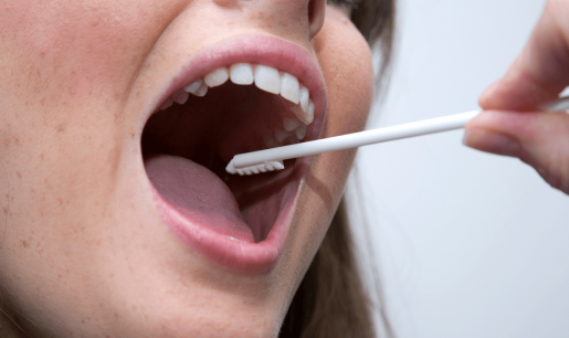 A person with their mouth open wide having their DNA collected via a mouth swab.