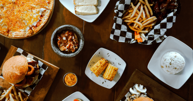 A collection of food, such as burgers and fries, pizza, chicken sings, roasted corn and rice. The food is placed on a table and shot from above.