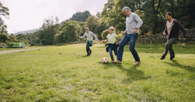 A family is playing soccer together in a field. There are two boys and their fathers