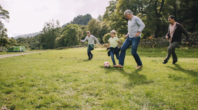 A family is playing soccer together in a field. There are two boys and their fathers