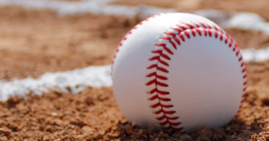 A closeup shot of a baseball resting on a dirt baseball feild.