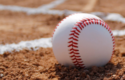 A closeup shot of a baseball resting on a dirt baseball feild.