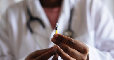 A doctor holding a needle with the tip pointed up. A yellow liquid sits in the syringe