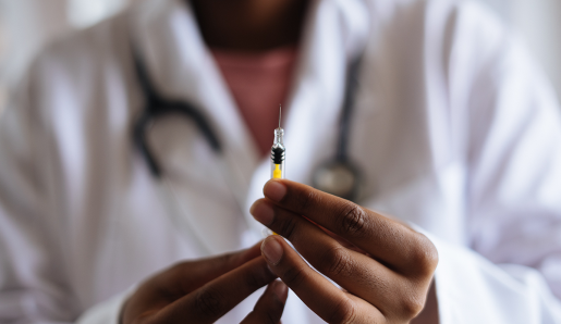A doctor holding a needle with the tip pointed up. A yellow liquid sits in the syringe