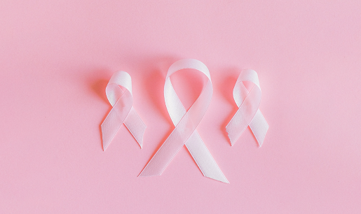 A display of three light-pink cloth ribbons. Each is looped at the top and folder over itself in the traditional breast cancer ribbon style. The three ribbons sit on a darker pink surface. The middle ribbon is larger, and the ones on either side are smaller.