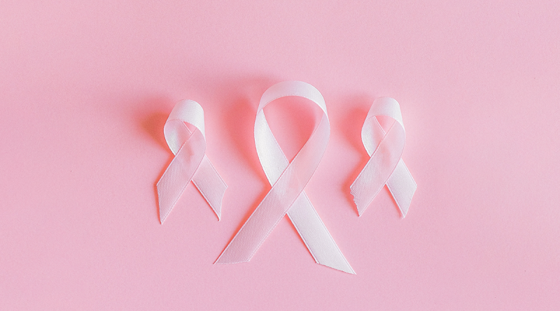 A display of three light-pink cloth ribbons. Each is looped at the top and folded over itself in the traditional breast cancer ribbon style. The three ribbons sit on a darker pink surface. The middle ribbon is larger, and the ones on either side are smaller.