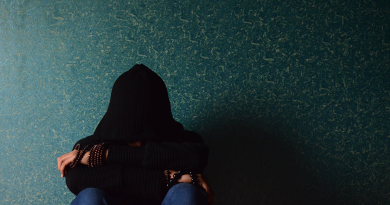 A person in a dark room sitting with a hoodie covering their face.