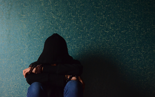 A person in a dark room sitting with a hoodie covering their face.