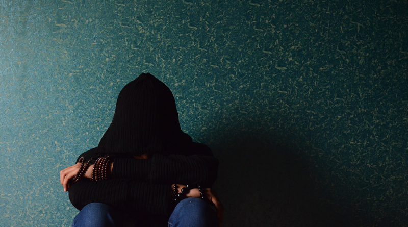 A person in a dark room sitting with a hoodie covering their face.
