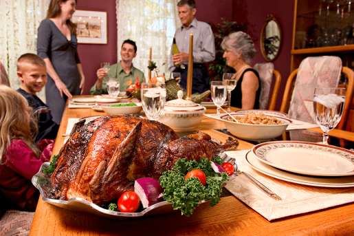 A holiday feast - turkey, dressing and vegetables. A family, including older people and children, sit around the table smiling.