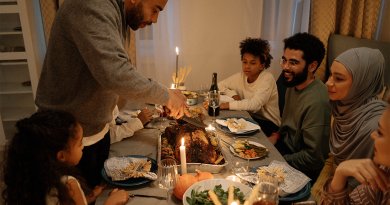 A family sitting around a candle-lit holiday meal, while one person stands to carve a turkey.