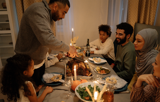 A family sitting around a candle-lit holiday meal, while one person stands to carve a turkey.