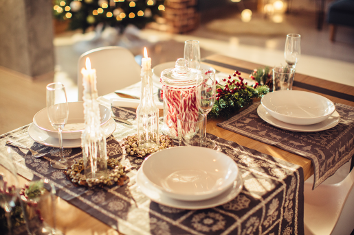 A holiday dinner table with plates and silverware laid out with a bunch of candy canes set in a glass jar in the middle of the table.