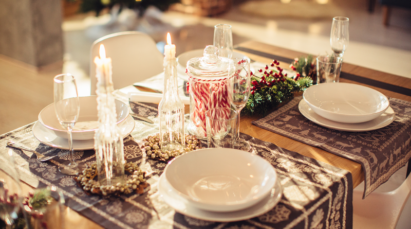 A holiday dinner table with plates and silverware laid out with a bunch of candy canes set in a glass jar in the middle of the table.