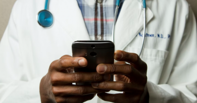 A doctor holding a smart phone with the camera pointed down, as if toward a patient.