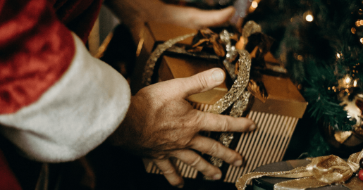 A Santa-suited hand placing a wrapped present under a Christmas tree.