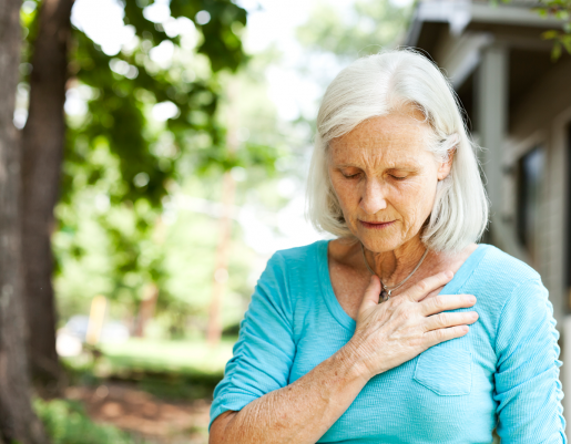 An older woman standing outside. She has a hand across her upper chest and a worried expression.