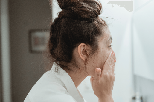 A woman looking into a mirror while cleansing her face