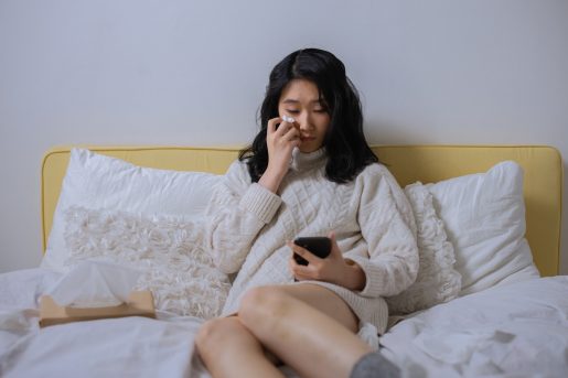 Woman sitting in bed crying while looking at her phone.