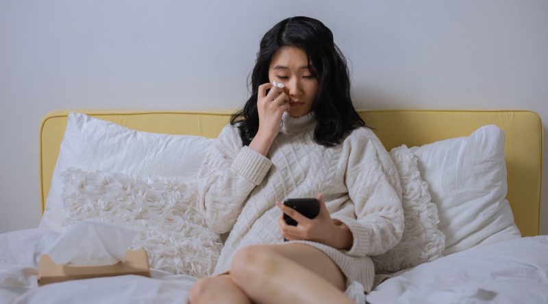 Woman sitting in bed crying while looking at her phone.